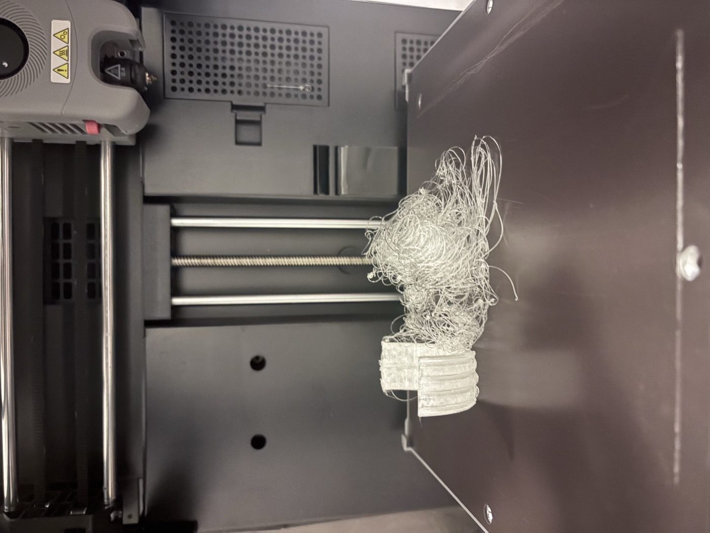 Photo inside a 3D printer: one half-printed clear tire and a large tangle of loose filament on the bed.